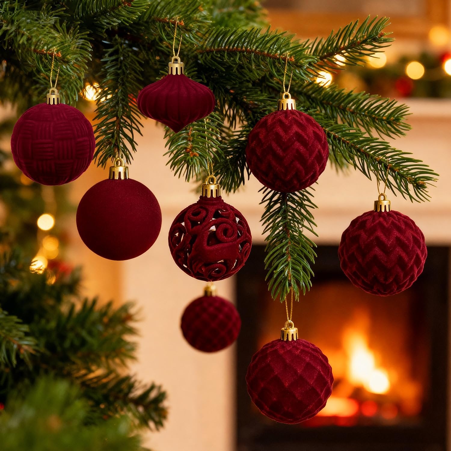 Burgundy flocked velvet Christmas ornaments hanging on a pine branch with a fireplace in the background.
