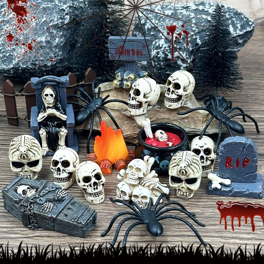 Halloween village figurines including skulls, spiders, a coffin, tombstone, and campfire on a wooden surface.