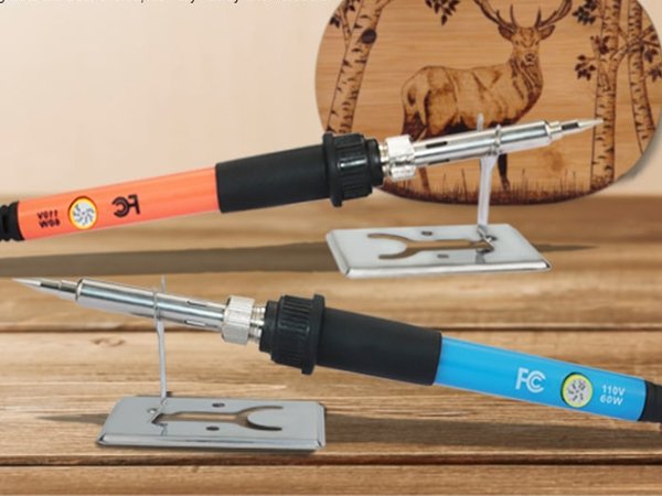 Two wood burning pens, one orange and one blue, resting on metal stands in front of a wooden plaque with a deer engraving.