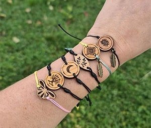 Close-up of a person's wrist wearing five wooden charm bracelets with nature and mystical symbols, outdoors.