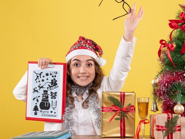 Woman in Santa hat holding stencil with Christmas designs and text, throwing glasses up near decorated tree and gifts