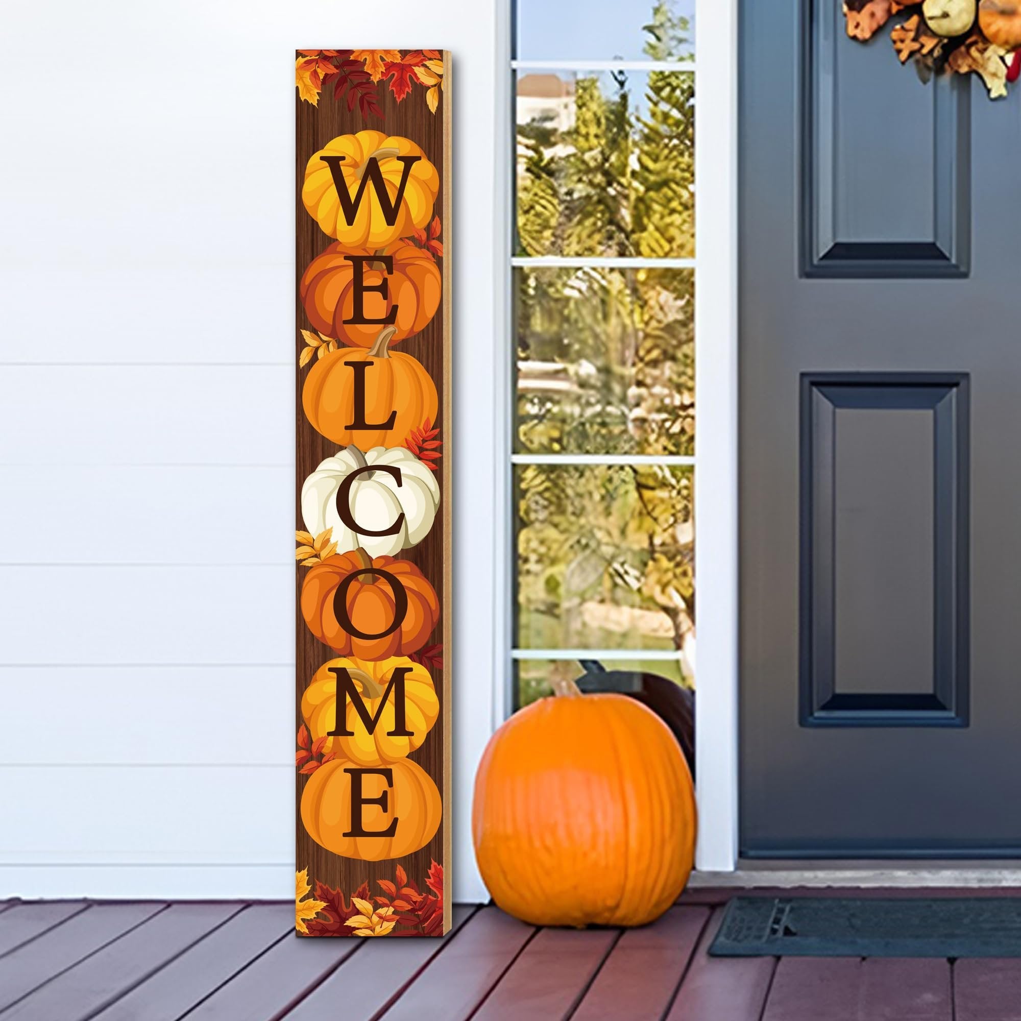 Vertical fall porch sign with pumpkins spelling WELCOME, decorated with autumn leaves, placed on a porch next to a real pumpkin.