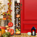 Wooden porch sign with 'hello FALL' text and autumn leaf graphics, displayed with pumpkins and a lantern.