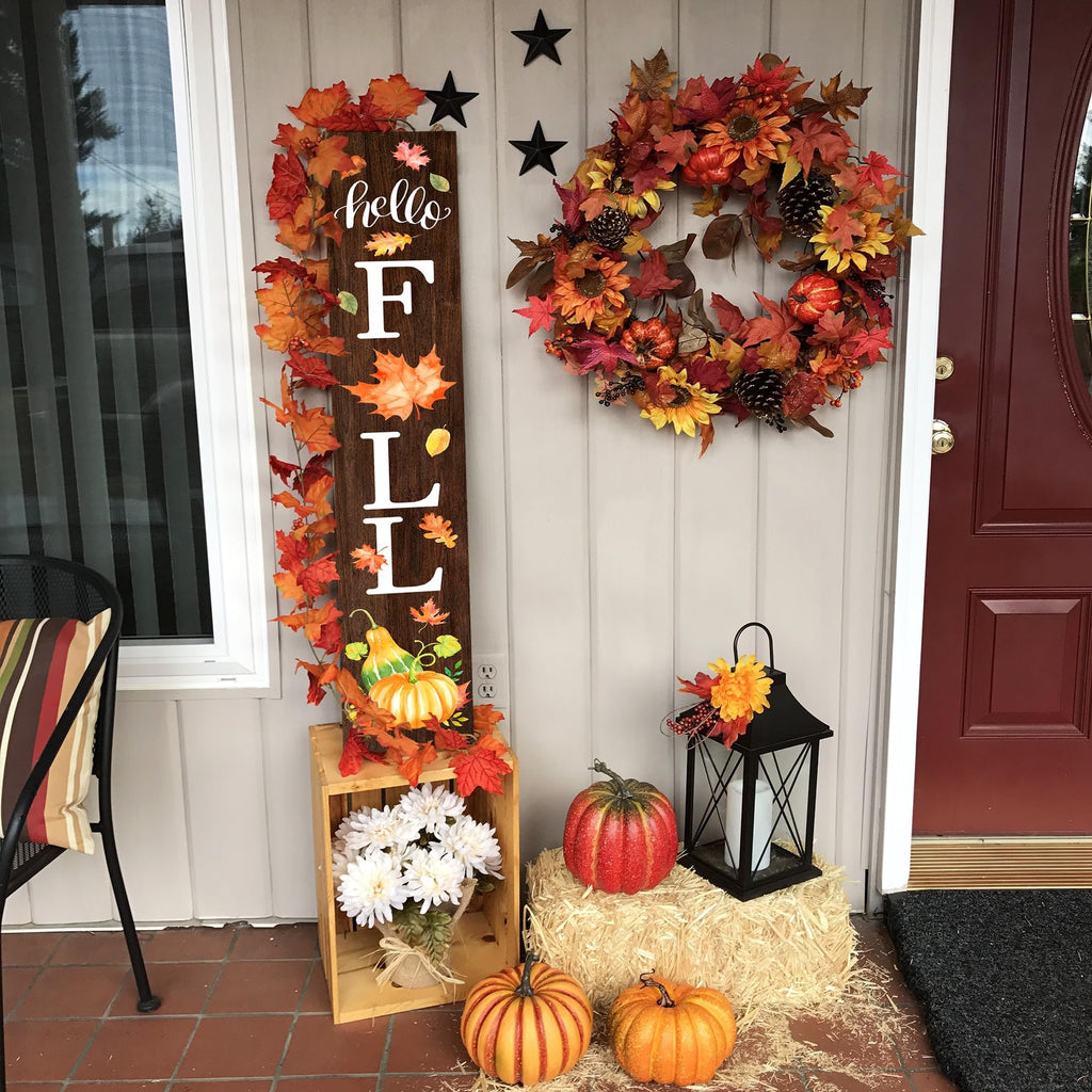 Wooden porch sign with 'hello FALL' text, autumn leaves, pumpkins, and a wreath, decorated for fall.
