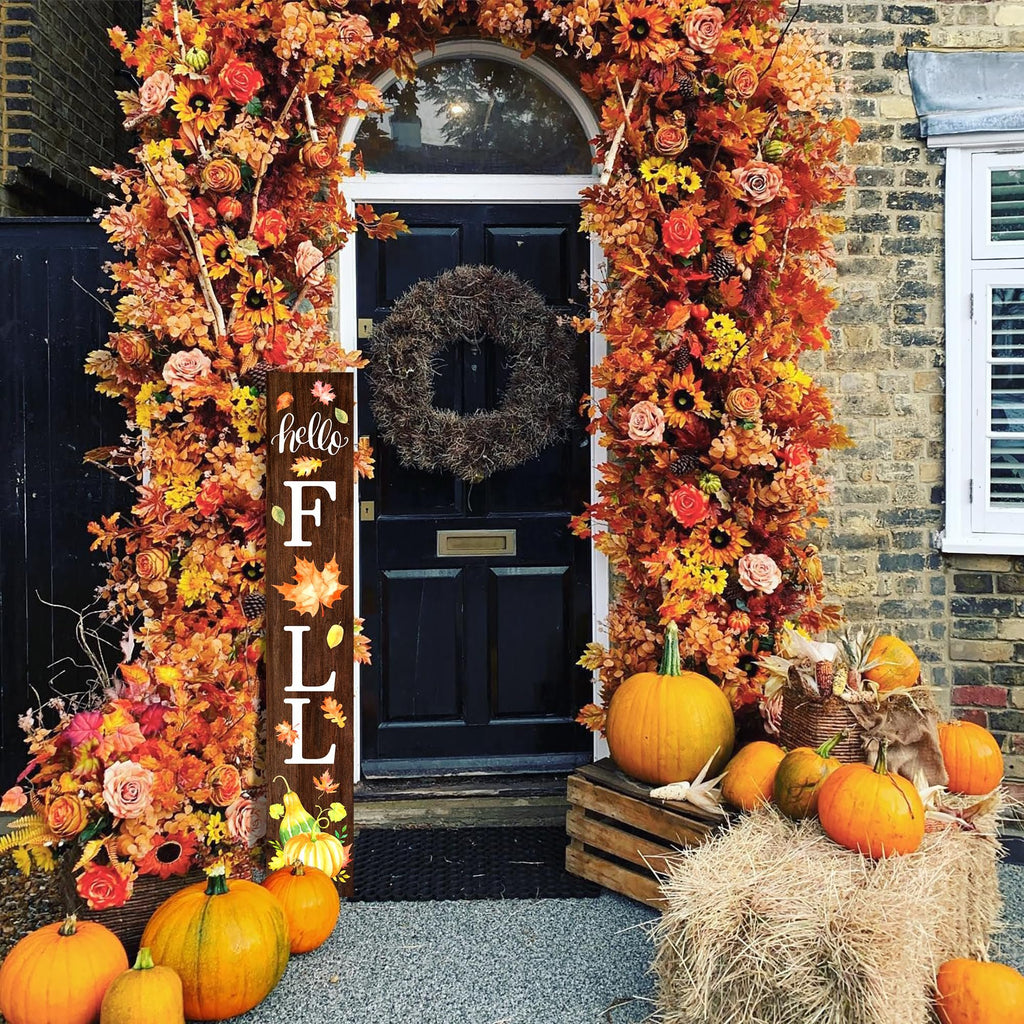 Wooden porch sign with 'hello FALL' text and autumn leaves, set against a decorated doorway with pumpkins and hay bales.