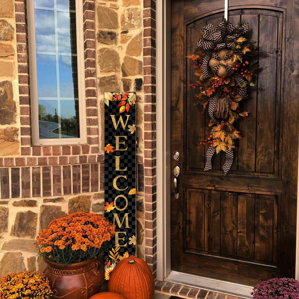 Vertical welcome sign with autumn leaves and pumpkins on a porch next to a door and flowers.