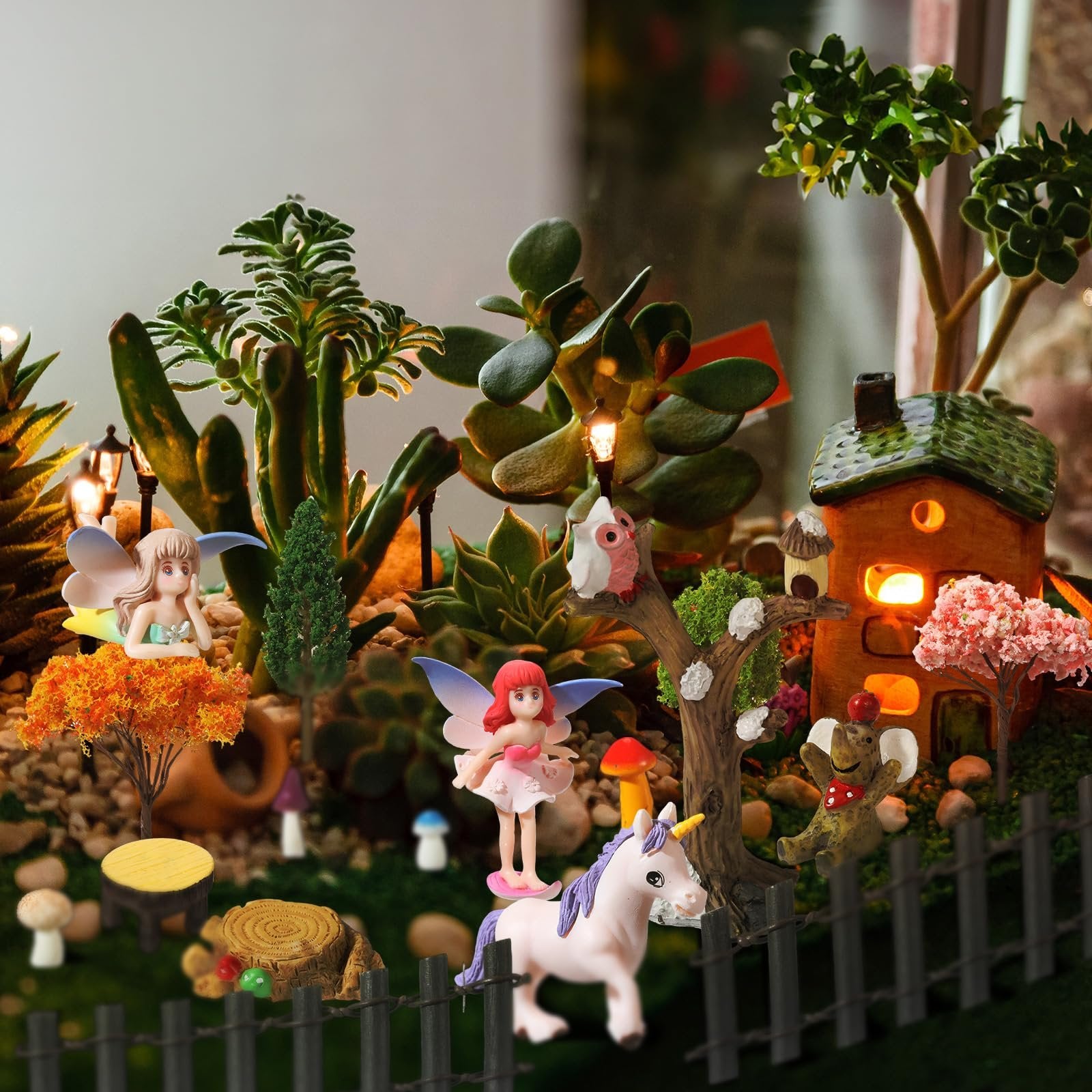 Miniature fairy garden scene with figurines, trees, house, and moss. Includes fairies, unicorn, owl, frog, and decorative plants.