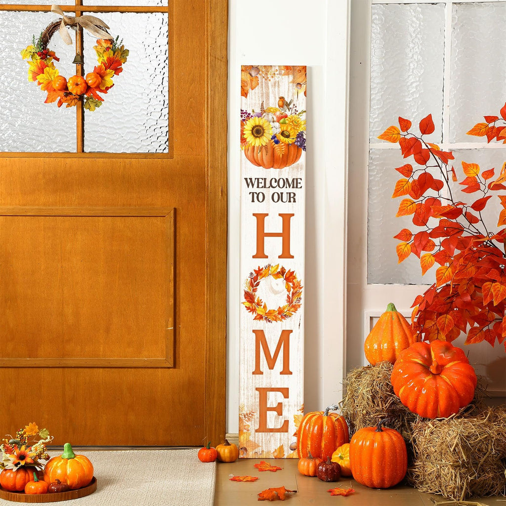 Front porch decorated for fall with a vertical welcome sign, pumpkins, hay bales, and a wreath on the door.