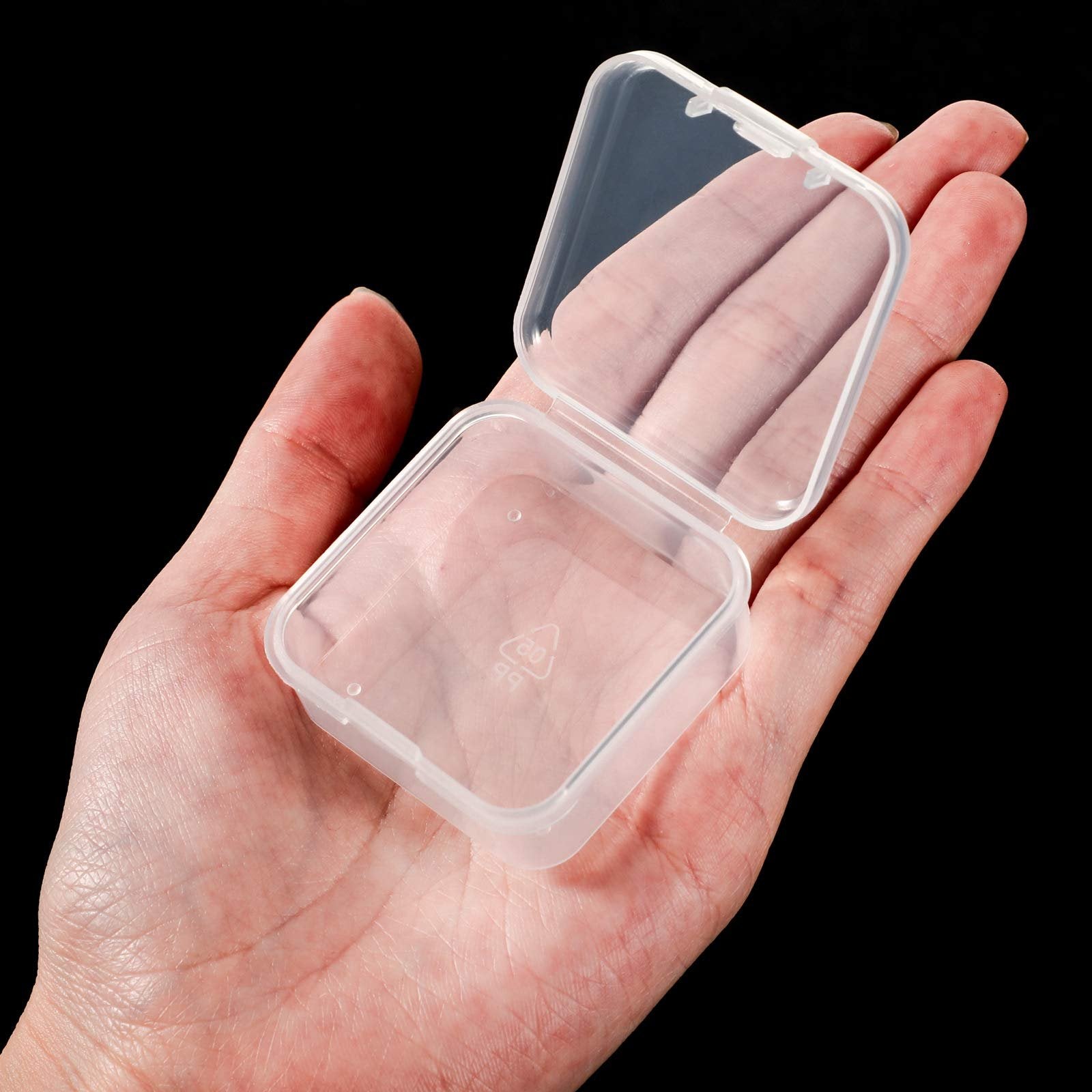 Hand holding an open, clear, square plastic storage box with a hinged lid. The box has a small recycling symbol embossed on the bottom.