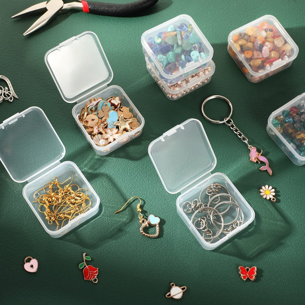Several clear plastic storage boxes filled with jewelry making supplies like beads, charms, and findings, arranged on a dark green surface with tools.