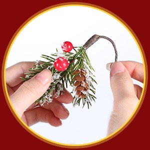Hands holding a faux pine branch with red berries and a pinecone, dusted with artificial snow.