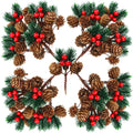 Four artificial pine branch sprays with pine cones and red berries arranged in a symmetrical pattern on a white background.