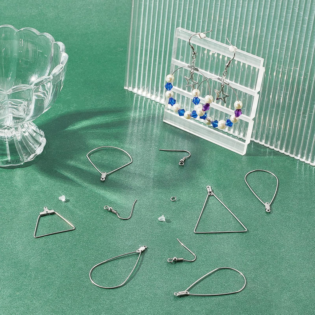 Stainless steel earring making components including hoops, hooks, jump rings, and ear nuts on a green surface.