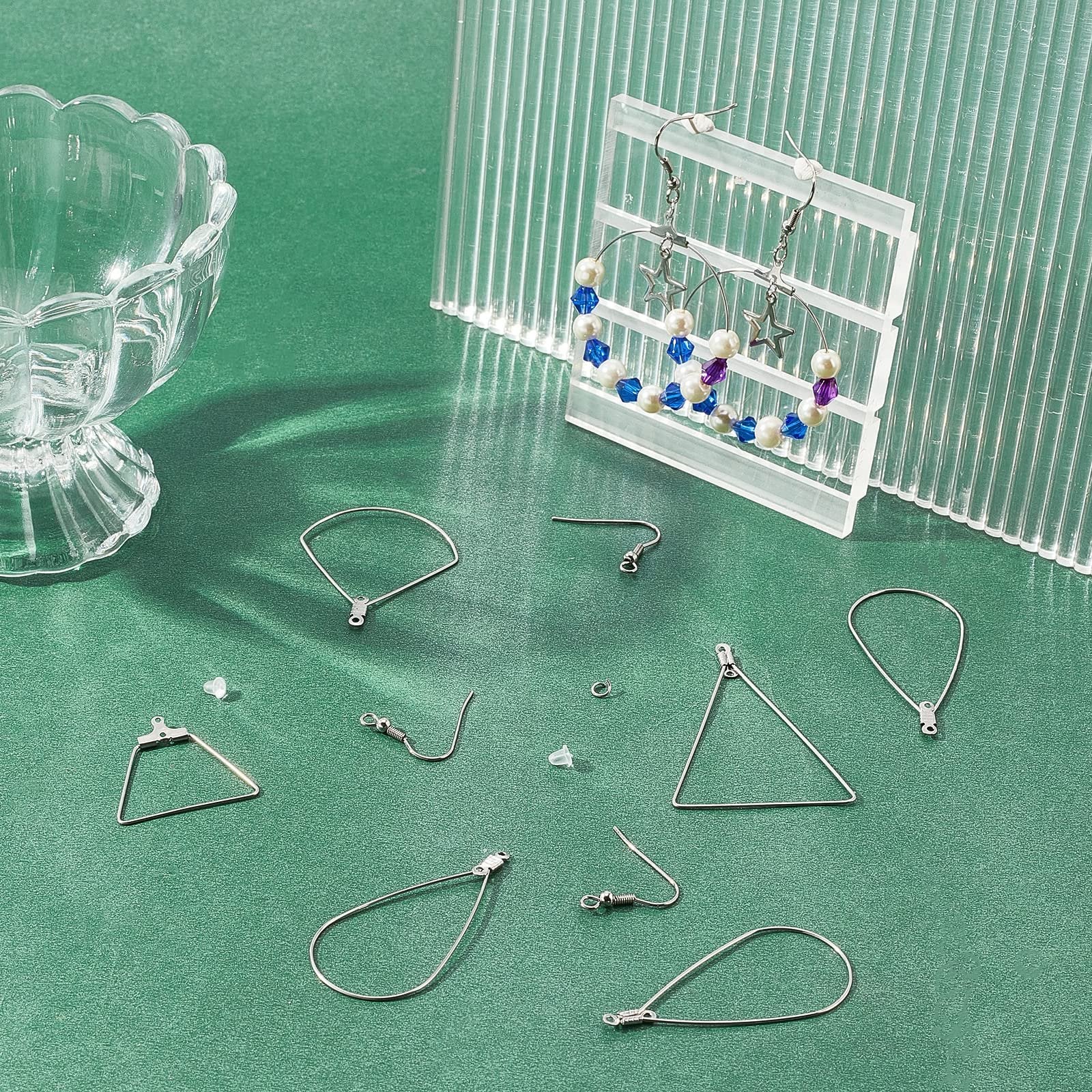 Stainless steel earring making components including hoops, hooks, jump rings, and ear nuts on a green surface.