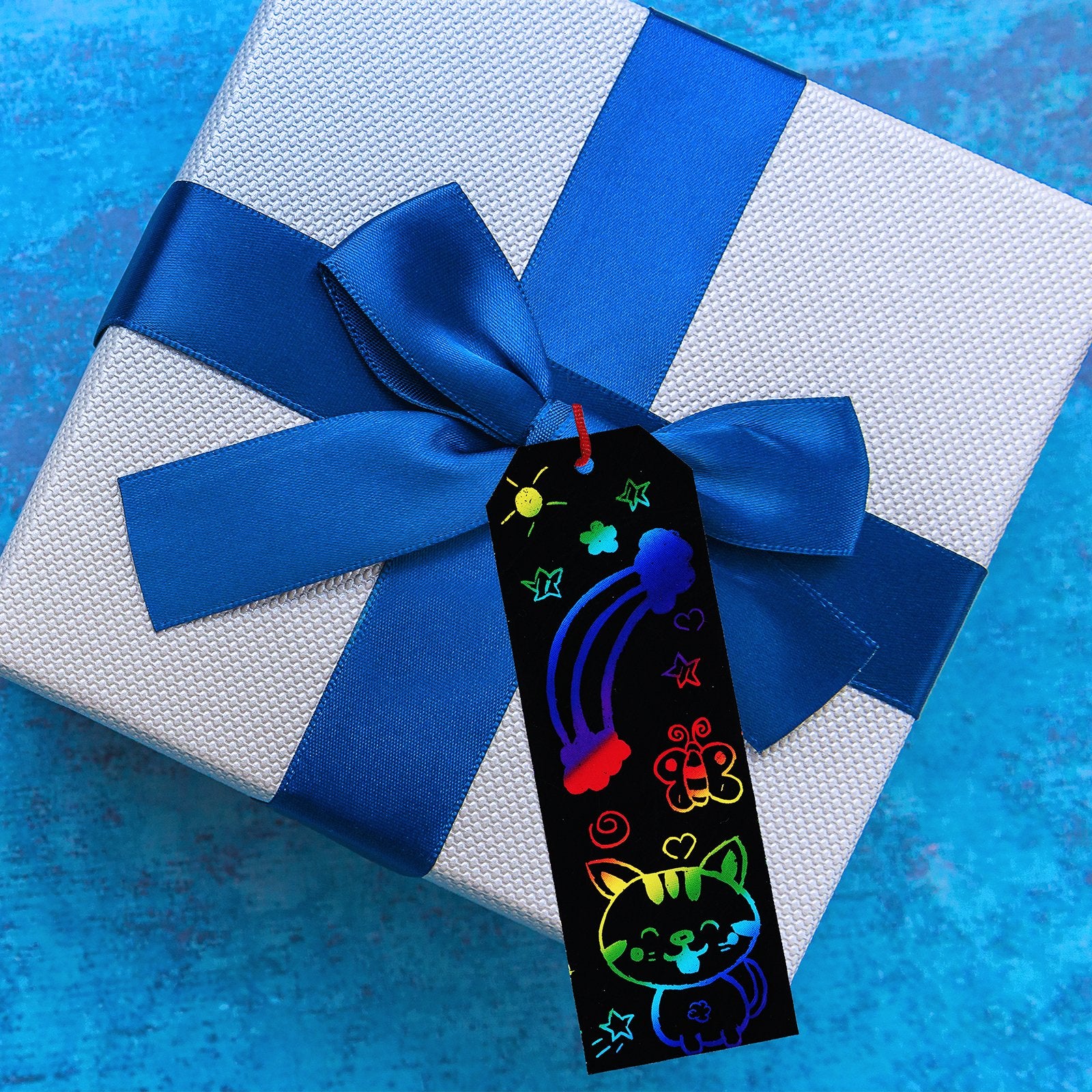 Scratch art bookmark with rainbow cat and butterfly designs on a gift box with blue ribbon