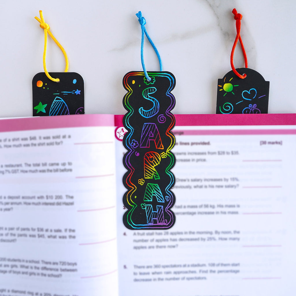 Rainbow scratch art bookmarks with colorful designs and cords, resting on an open book.