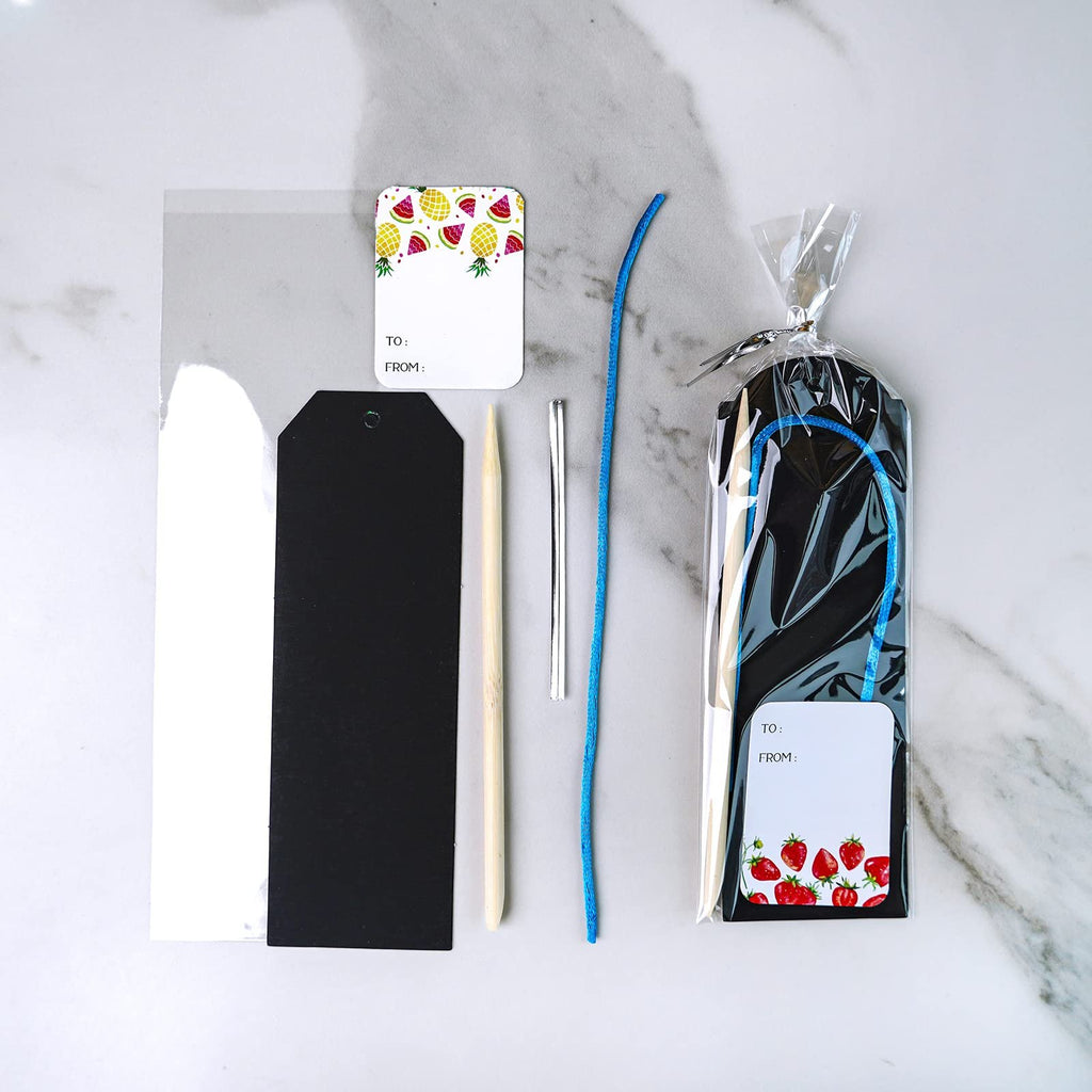 Scratch art bookmark craft kit contents including black and white bookmark blanks, wooden stylus, silver tool, blue cord, and gift tags with fruit designs.