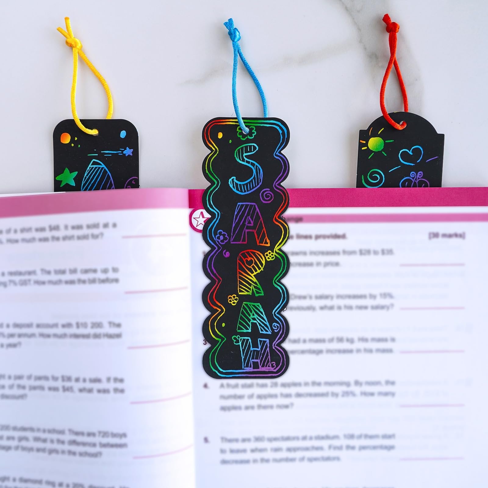 Rainbow scratch art bookmarks with colorful designs and cords peeking out of an open book.