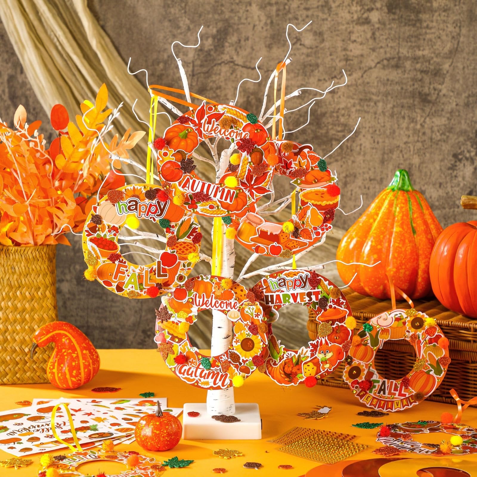 Autumn wreath craft kits displayed on a white tree stand with pumpkins and fall foliage in the background.