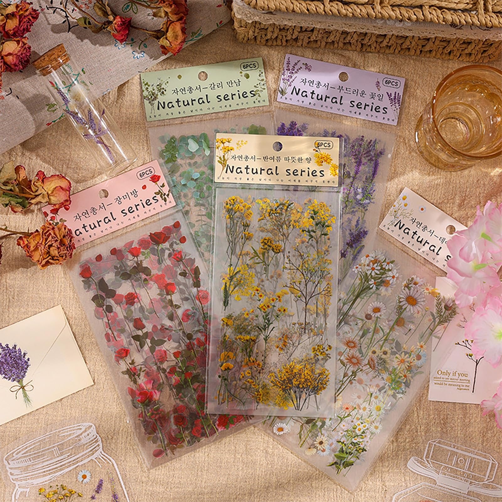 Collection of vintage botanical sticker sheets featuring roses, yellow wildflowers, and daisies, arranged on a textured surface with dried flowers.