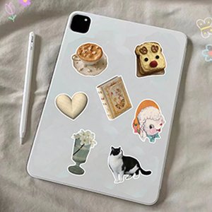 Various vintage aesthetic vinyl stickers applied to a tablet device, including a coffee cup, toast, heart, book, girl, vase, and cat.