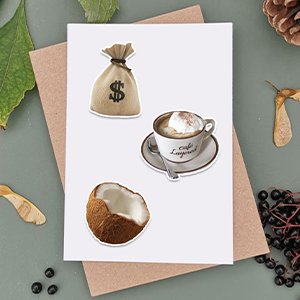 Three vinyl stickers on a white card: a money bag with a dollar sign, a cup of coffee, and half a coconut.