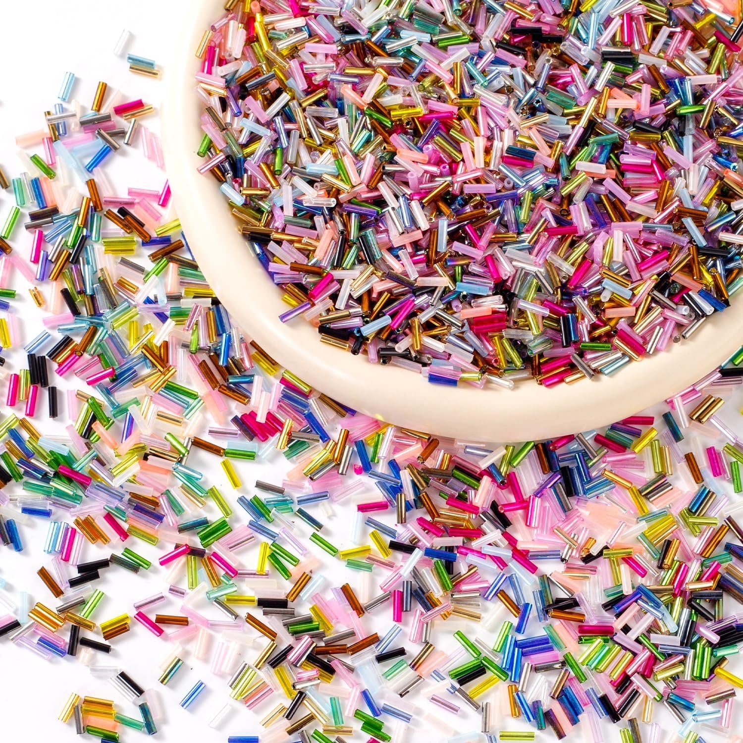 Close-up overhead view of colorful 7mm glass tube beads spilling from a light-colored bowl onto a white surface.