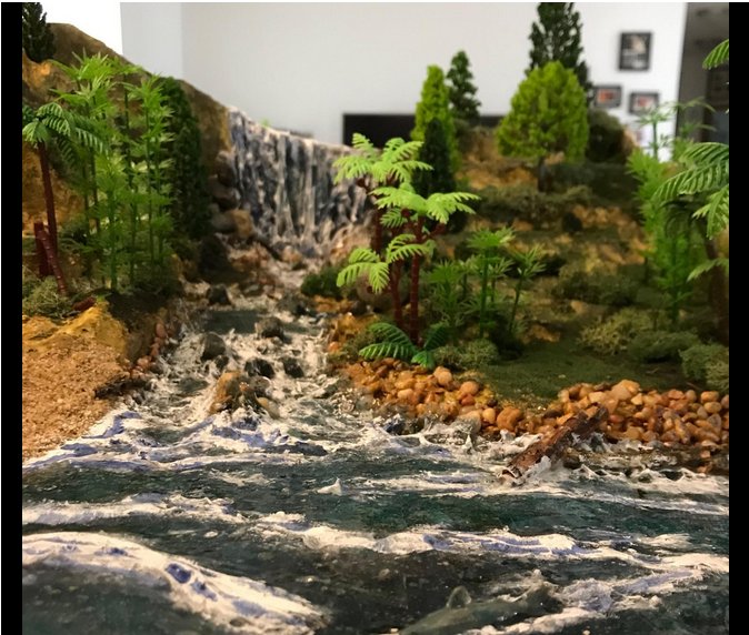 Diorama scene with a waterfall flowing into a river, surrounded by trees, bushes, and rocks.