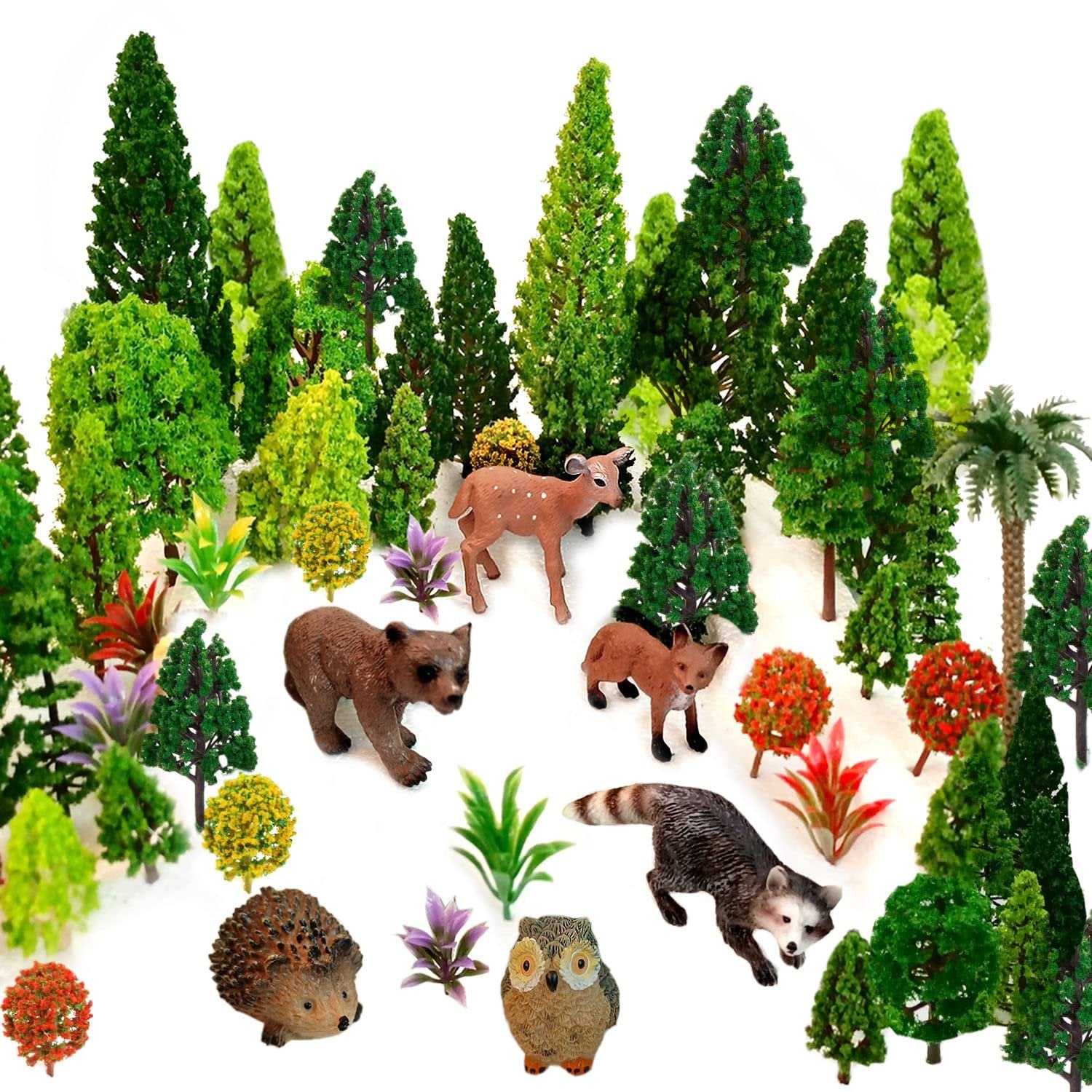 Assortment of miniature plastic forest animals and trees on a white background.