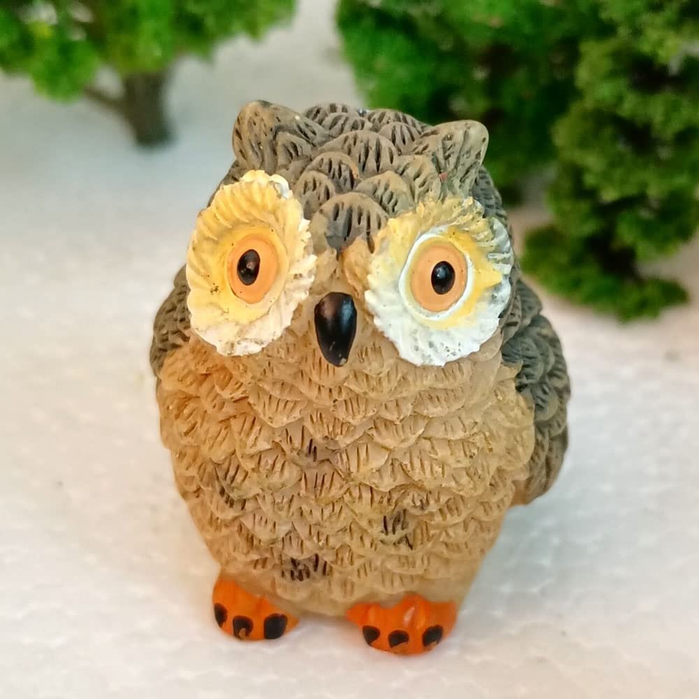 Plastic owl figure with large yellow eyes and orange feet, set against a blurred green foliage background.