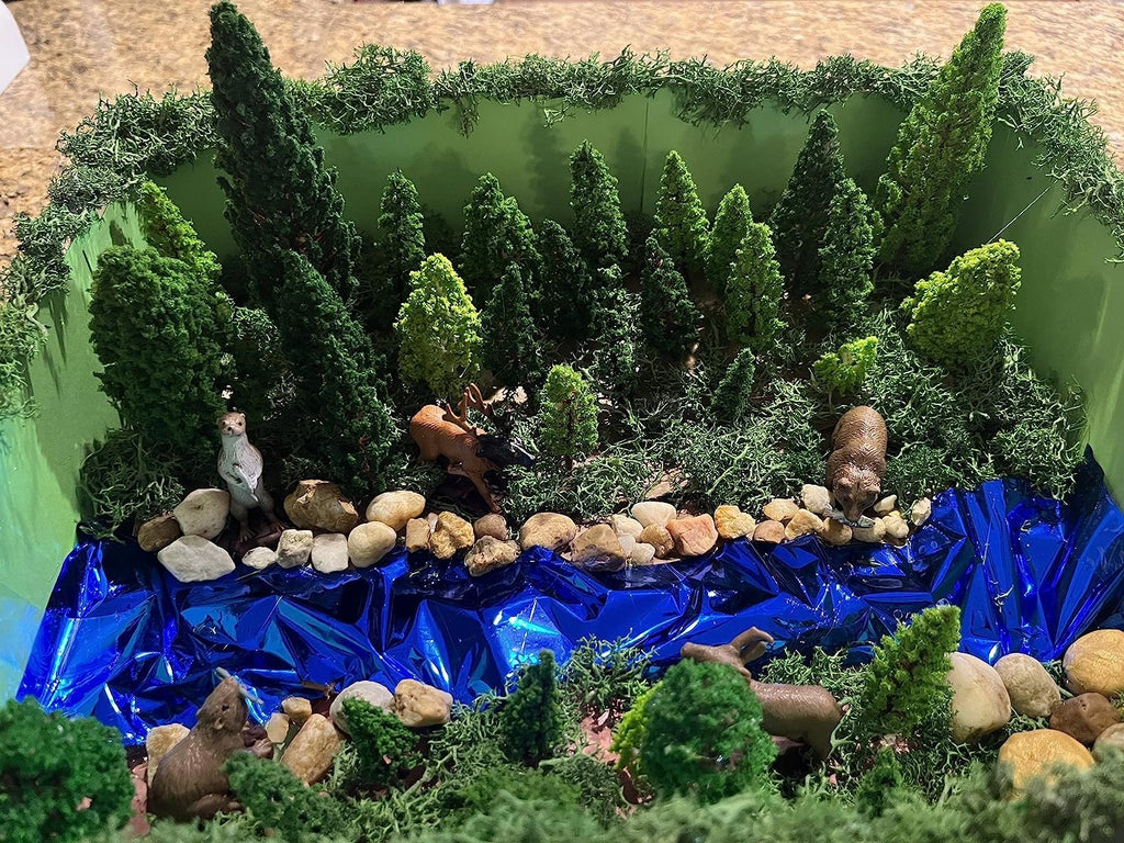 Diorama scene with miniature trees, rocks, animals, and a blue river, set in a green box.