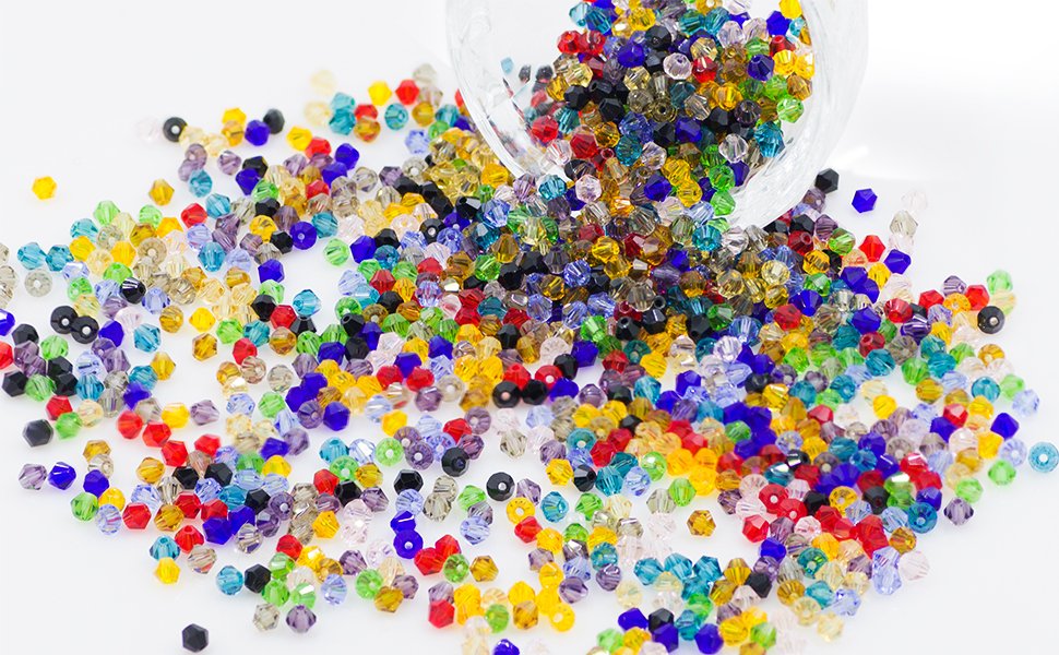 Assorted faceted bicone crystal glass beads spilled from a clear bowl onto a white surface, showing 14 colors.