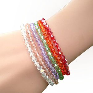 Assorted faceted bicone crystal glass beads in multiple colors arranged on a wrist.
