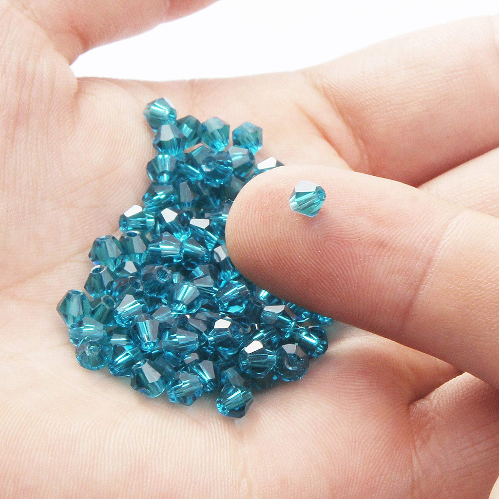 Hand holding a pile of faceted bicone crystal glass beads in teal blue color.