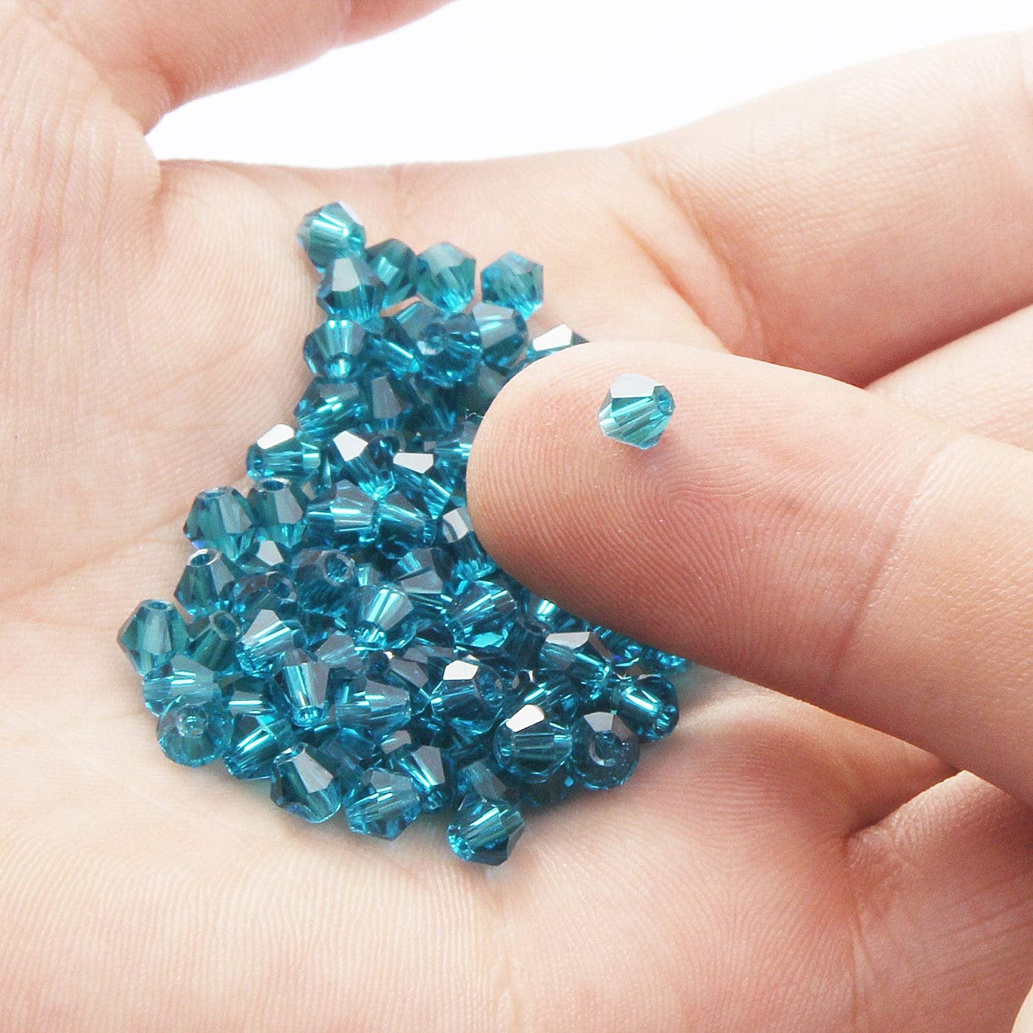 Hand holding a pile of faceted bicone crystal glass beads in teal blue color.