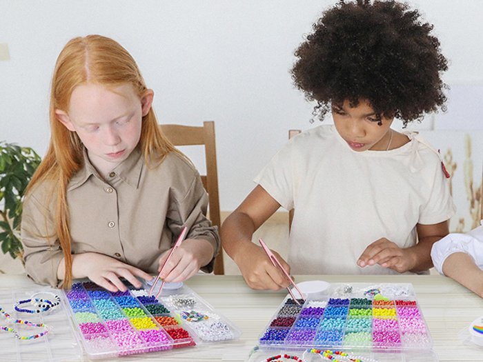 Two children making jewelry with colorful seed beads and charms from a kit.