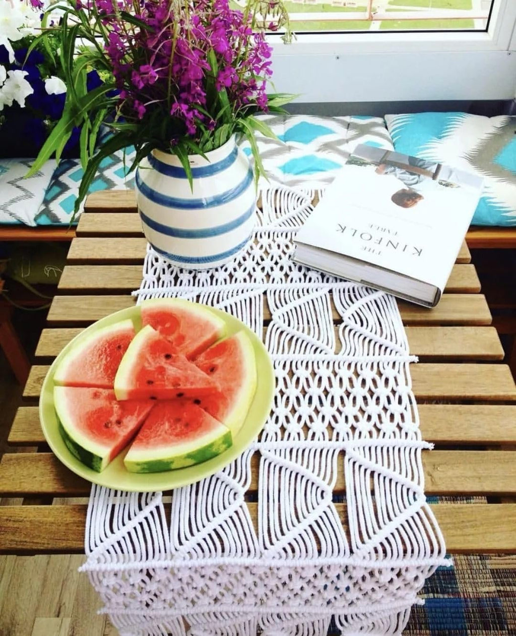 White macrame table runner with intricate pattern, topped with a plate of watermelon slices and a vase of flowers.