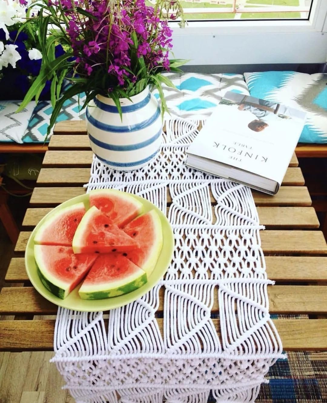 White macrame table runner with intricate pattern, topped with a plate of watermelon slices and a vase of flowers.