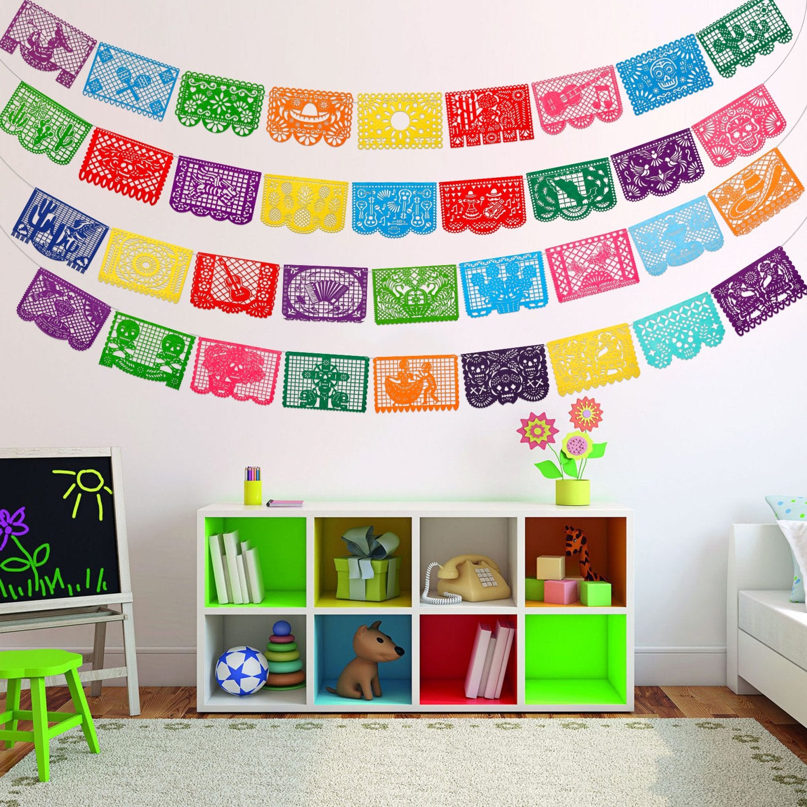 Colorful Papel Picado banners hanging on a white wall above a shelf with toys and books.