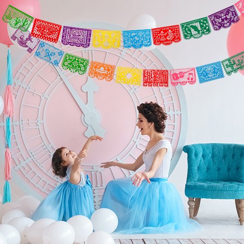 Mother and daughter in blue dresses playing with colorful papel picado banners in a festive room