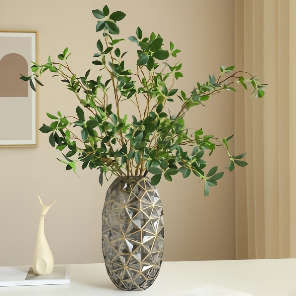 Faux ficus twig branches with green leaves in a decorative vase on a table.