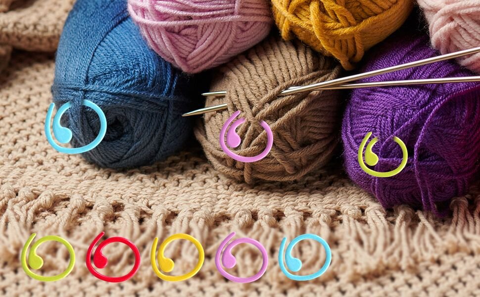 Crochet stitch markers in various colors on yarn balls and a textured fabric.