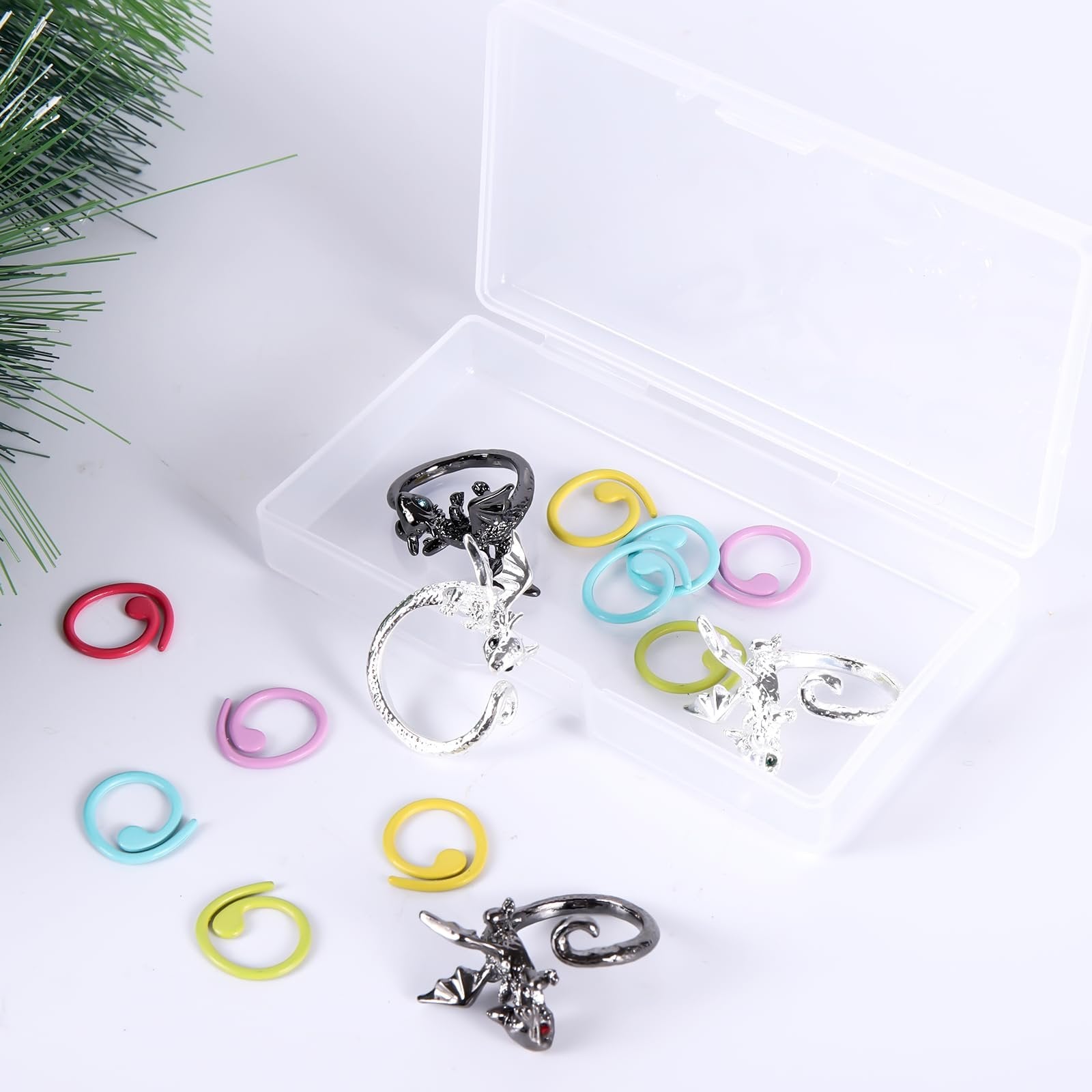 Dragon-shaped crochet rings and colorful stitch markers scattered around a clear plastic box.