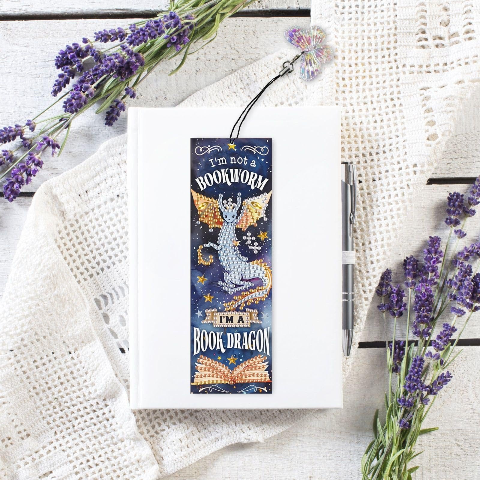Diamond art bookmark kit with dragon design and rhinestone tassel on a white book with lavender sprigs
