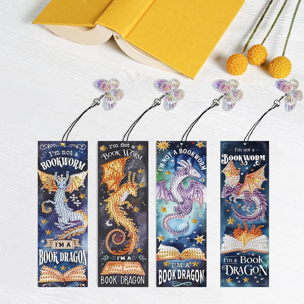 Four diamond art bookmark kits with dragon designs and rhinestone tassels, laid out with a yellow book and decorative orbs.