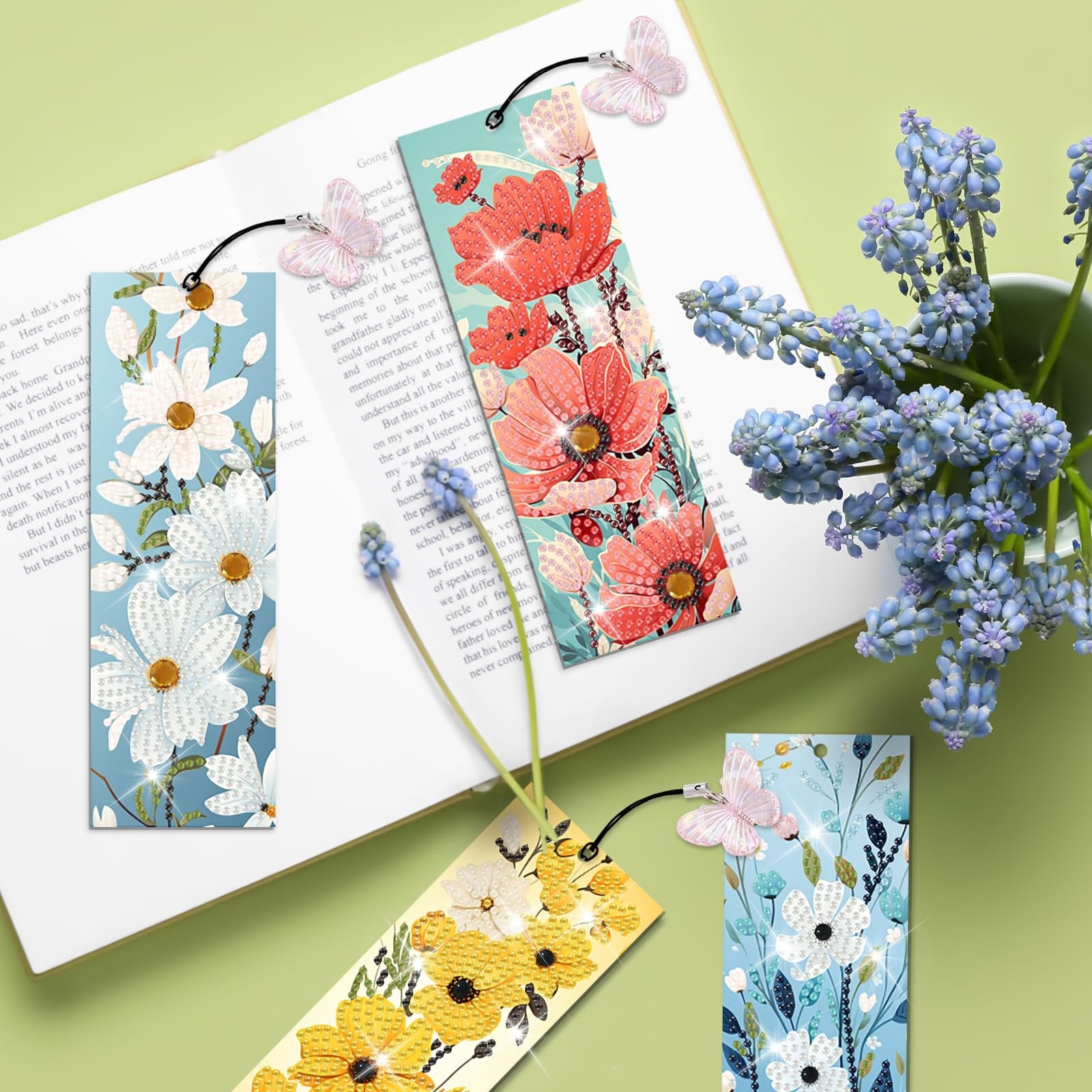Diamond art bookmarks with floral designs and butterfly charms resting on an open book, next to blue flowers.