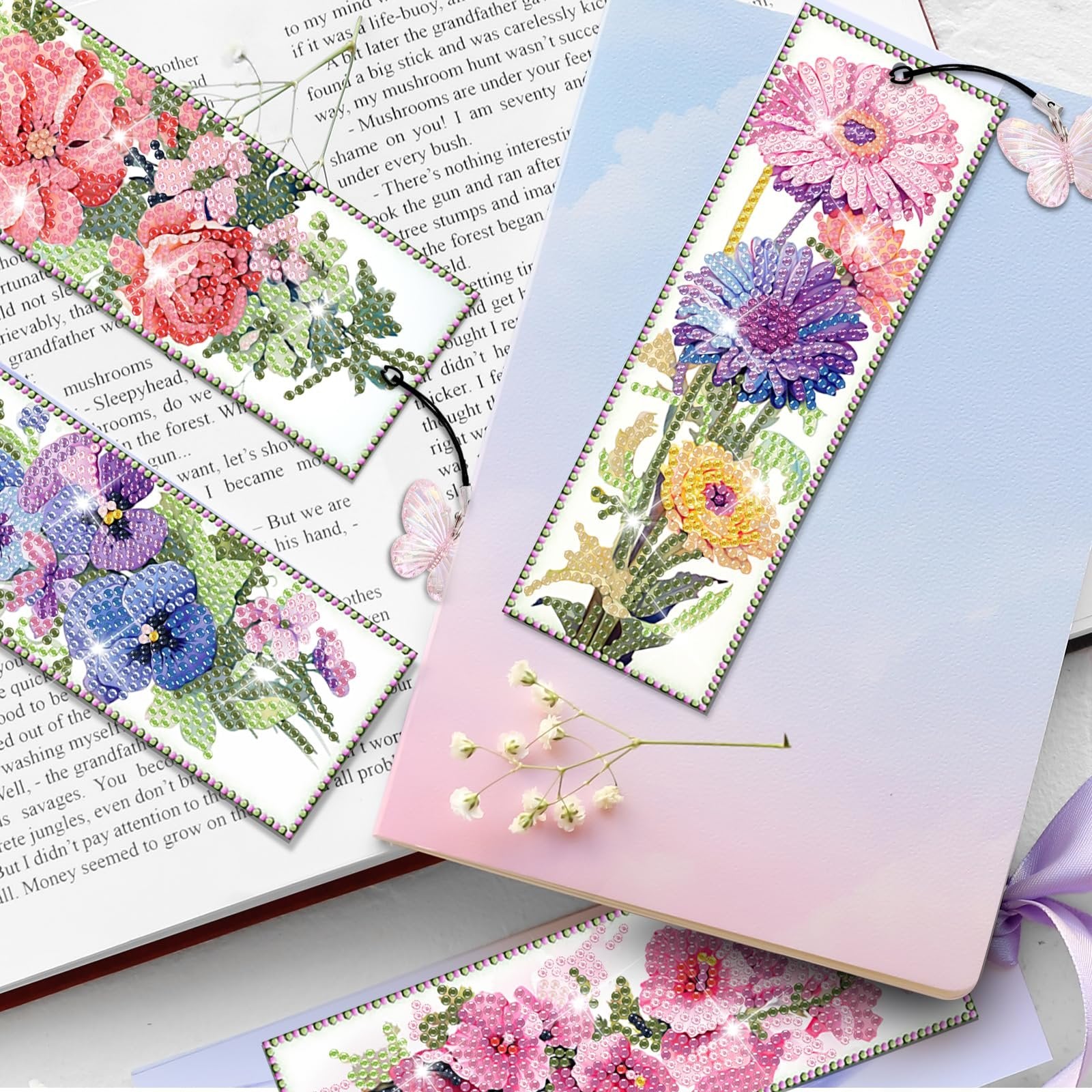 Diamond art bookmarks with floral designs laid on an open book and notebook.