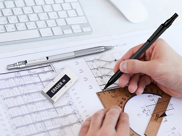 Person drafting with mechanical pencils and eraser on blueprints, with keyboard and mouse in background.