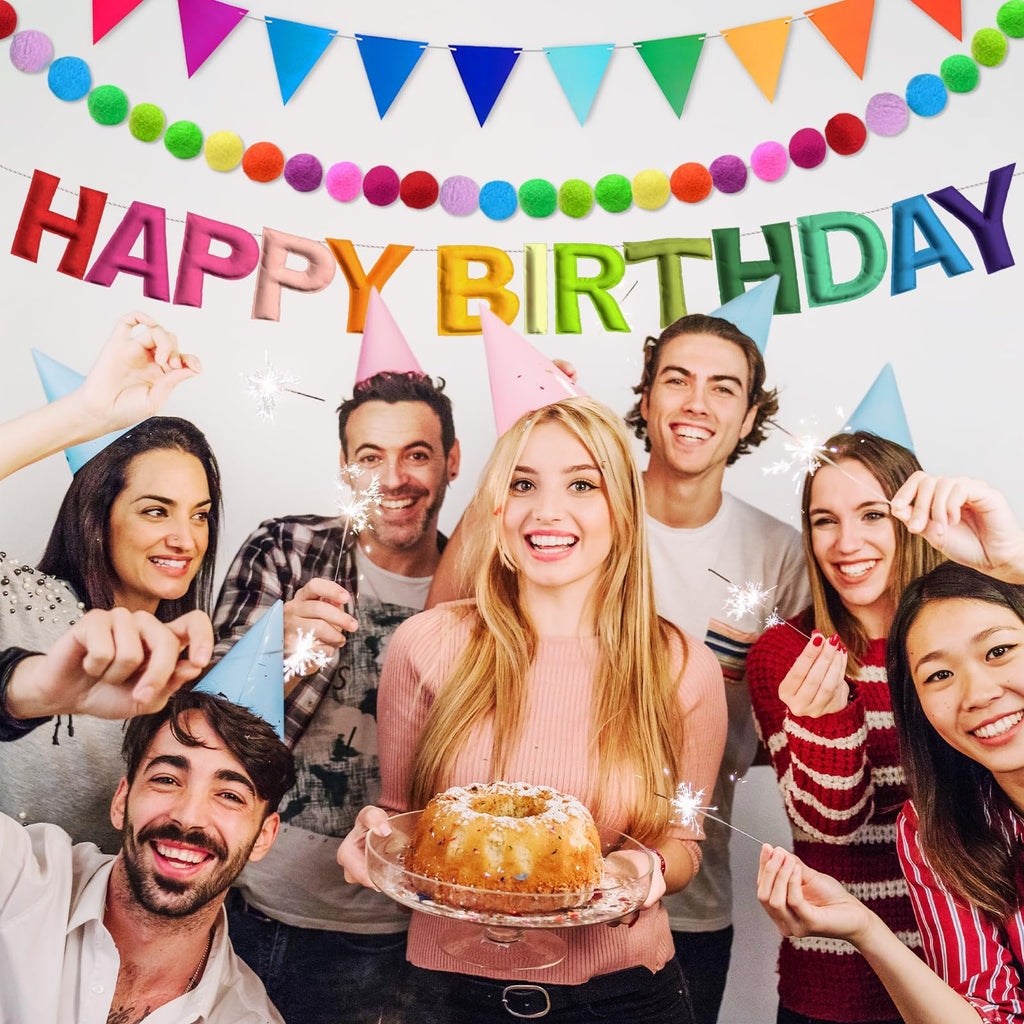 Group of friends celebrating a birthday with sparklers and a cake, wearing party hats, with colorful banners in the background.
