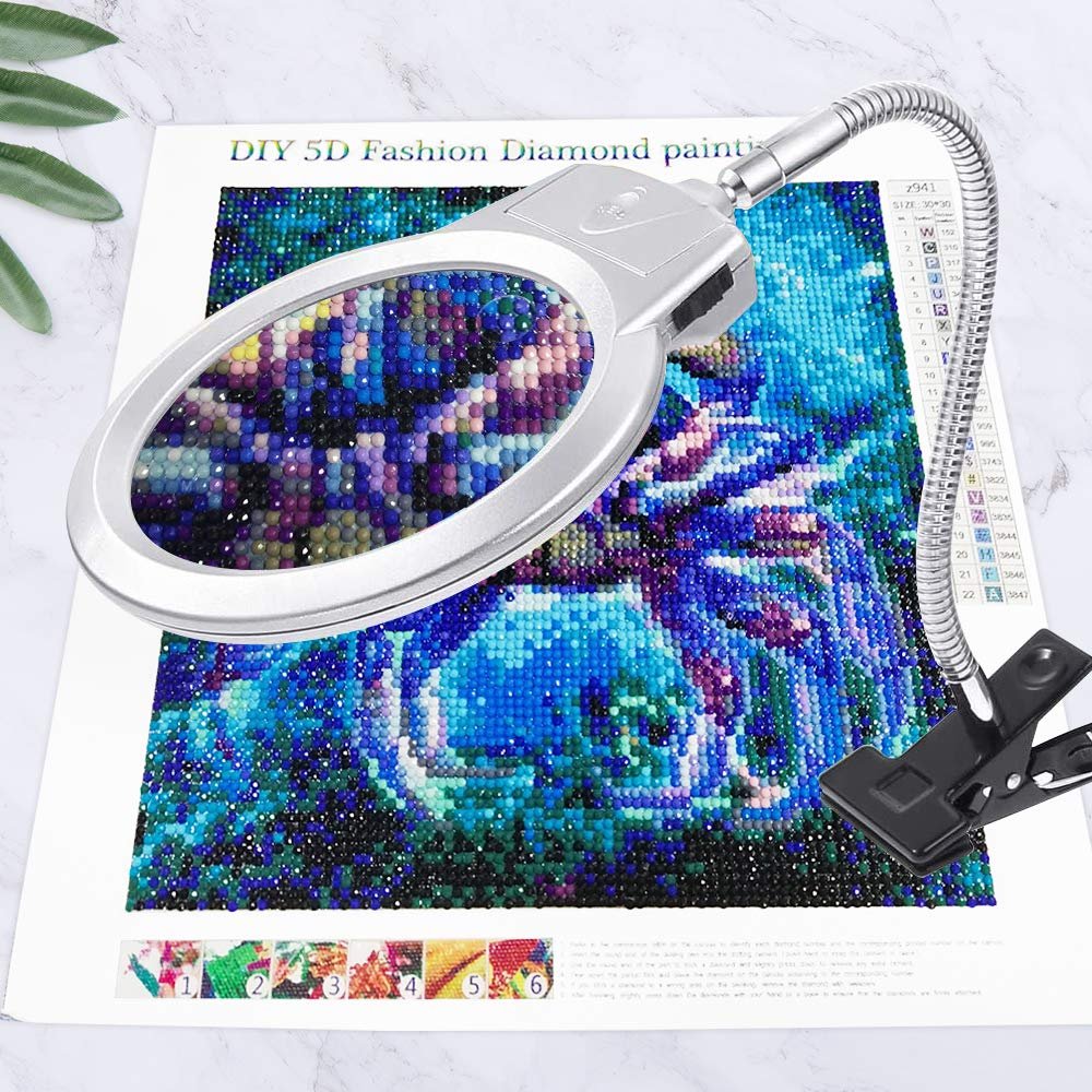 Diamond painting magnifier with clamp positioned over a colorful diamond painting kit.